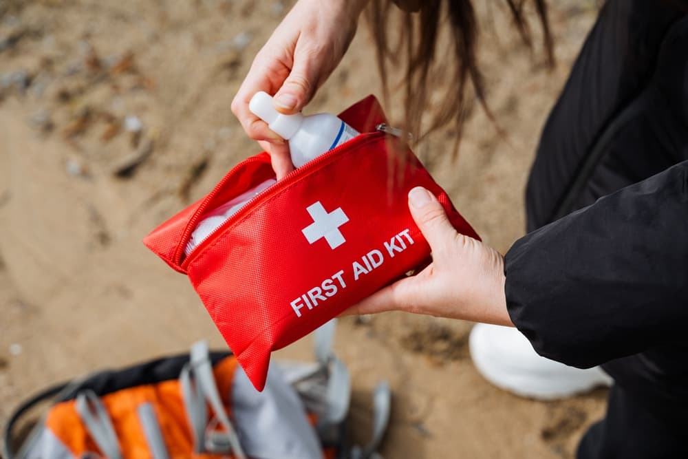 Hands using a red first aid kit outdoors, showing readiness for emergencies during hiking, camping, or travel. Essential medical supplies for outdoor safety.