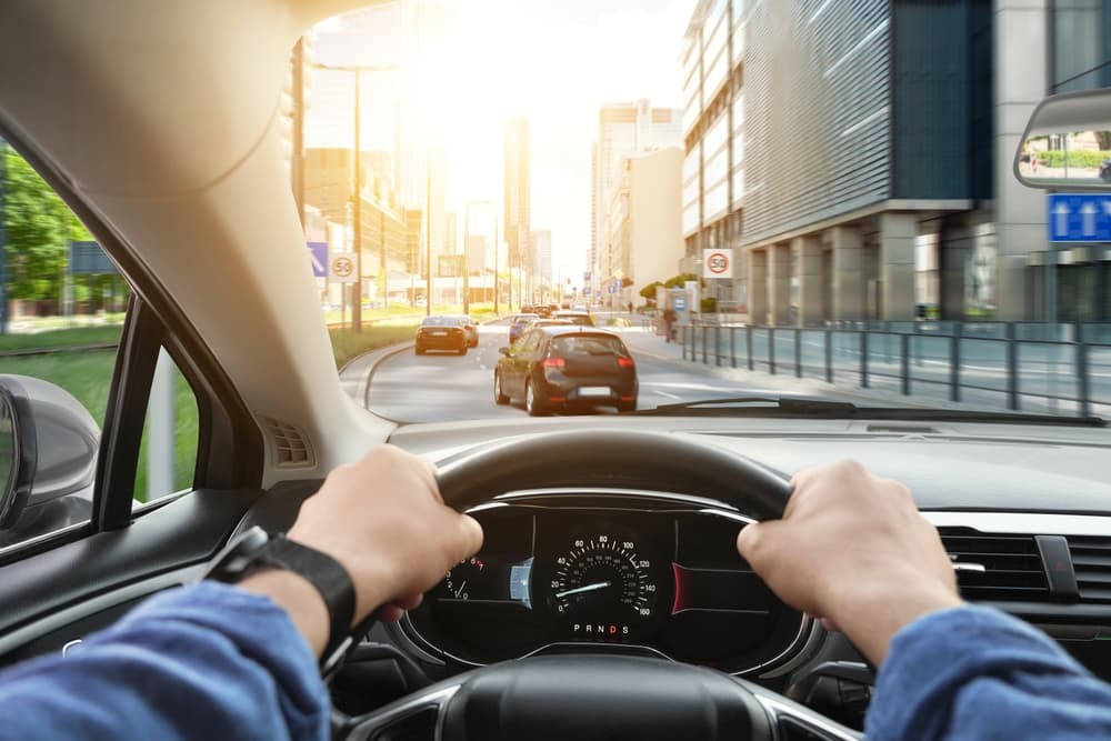 Driving a car with a closeup view from the driver’s seat—man’s hands firmly gripping the steering wheel, focused on the road ahead.