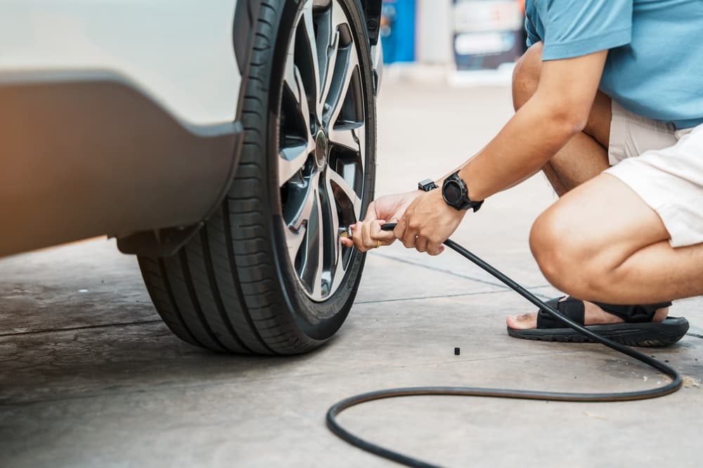 Man inflating car tire at gas station, removing valve cap to check air pressure and fill with nitrogen. Self-service maintenance for safety and performance.