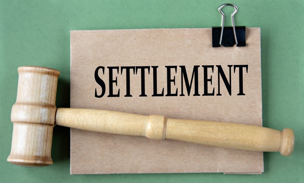 Wooden gavel next to a folder labeled settlement, symbolizing legal case resolution