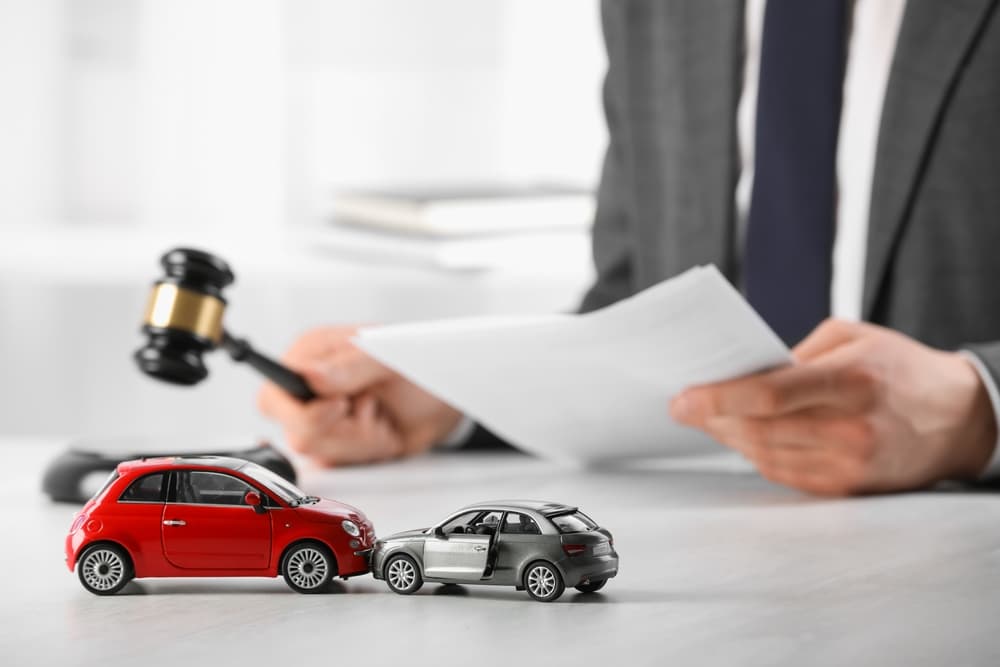 Auto accident law concept: A lawyer with legal documents and gavel at a table, with focus on toy cars in the foreground.