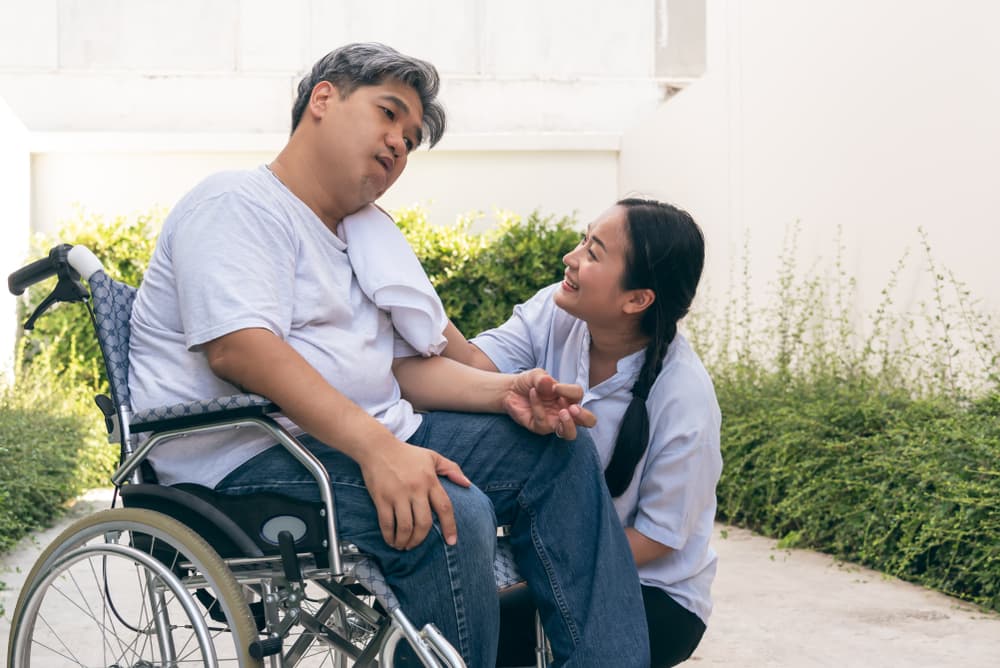 A devoted wife attends to her husband seated in a wheelchair, coping with the challenges of neurological diseases.