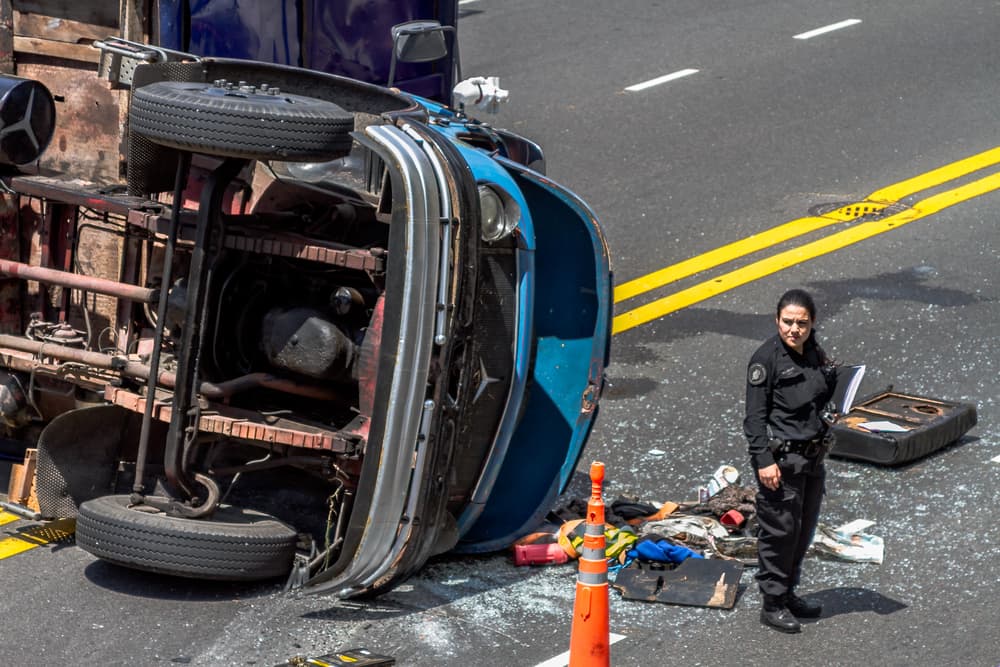 Female police officer managing traffic post-accident in front of a dump truck, ensuring safety and order at the scene.