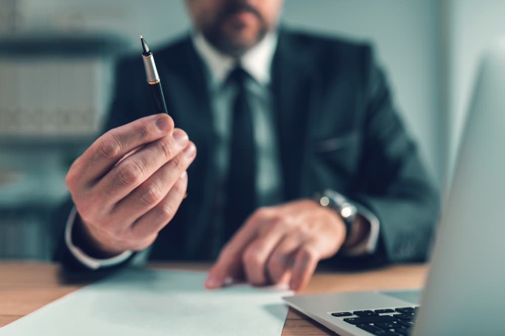 Selective focus image of an insurance agent offering a pen to a client for signing a document.