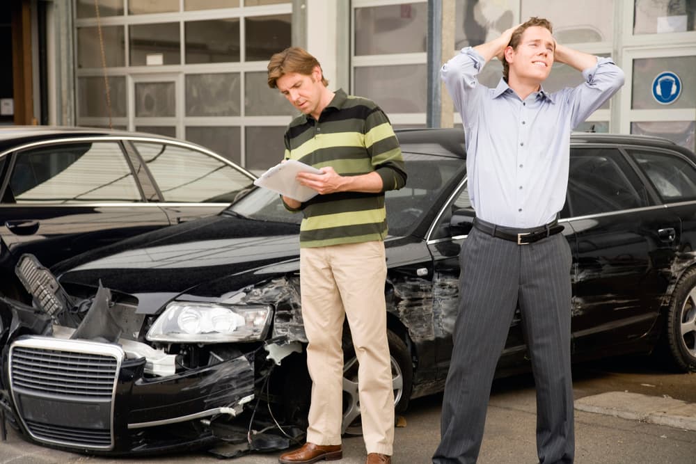 Car owner in distress while insurance adjuster assesses car damage.