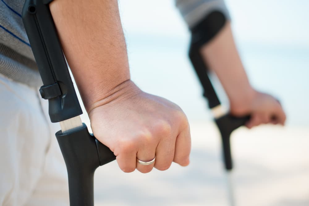 A man with leg injury uses crutches to walk on the beach, facing challenges due to his truck accident injury.