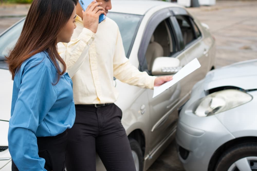 Two drivers exchanging contact information and insurance details on smartphones after a car accident, illustrating the process of online insurance claims.