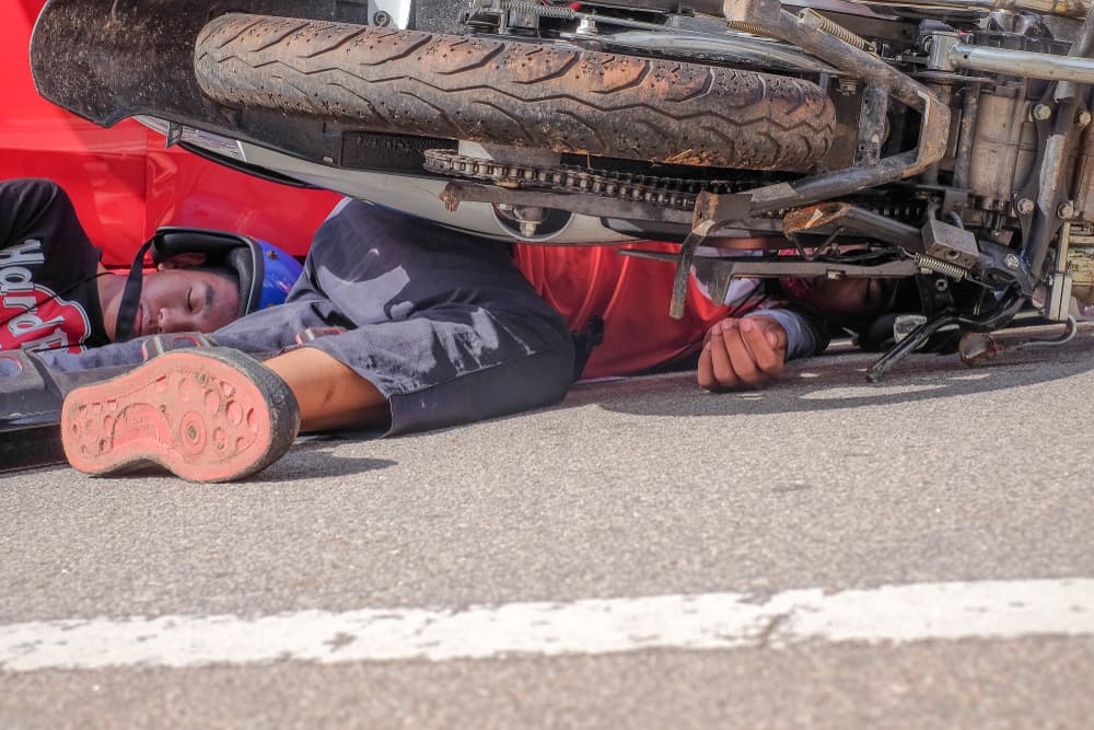 Injured motorcyclists lying on the road following an accident.
