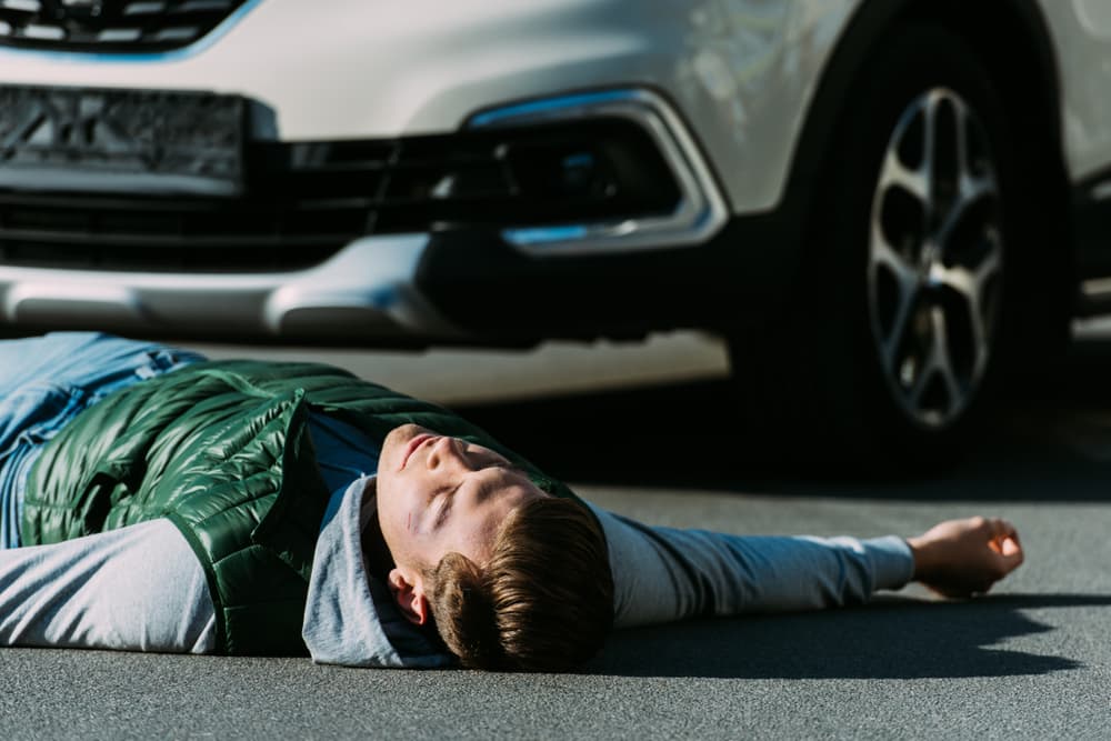 A close-up view of a young man lying injured on the road after a car accident.
