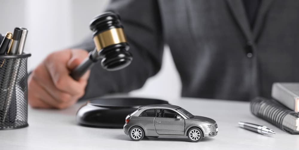 Close-up of judge striking a gavel beside a toy car, symbolizing legal action in auto accident cases. Ideal for banner or legal-themed design.