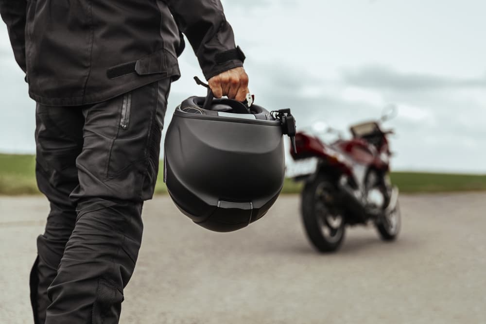 A man approaches his motorcycle, carrying a helmet in his hands. Close-up shot of the motorcycle helmet.