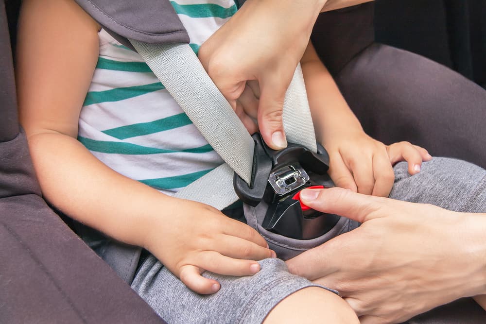 A woman fastens a seatbelt for her child in a car seat. The toddler is ready for a summer trip, highlighting vehicle safety and transportation awareness.