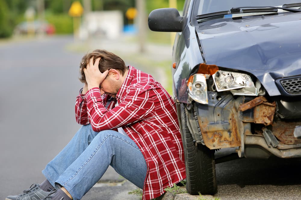 Injured man rests beside wrecked vehicle after collision.
