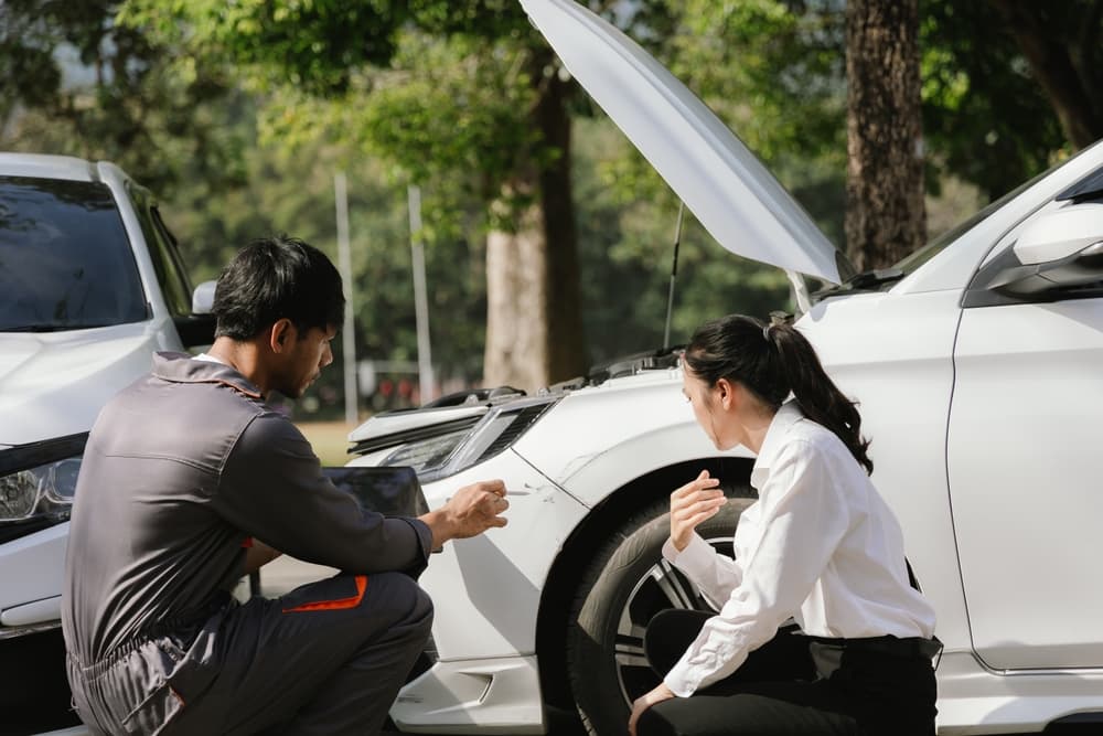 Insurance agents assist clients outdoors after a car accident—inspecting vehicle damage, reviewing coverage, discussing repairs, liability, and filing a claim.