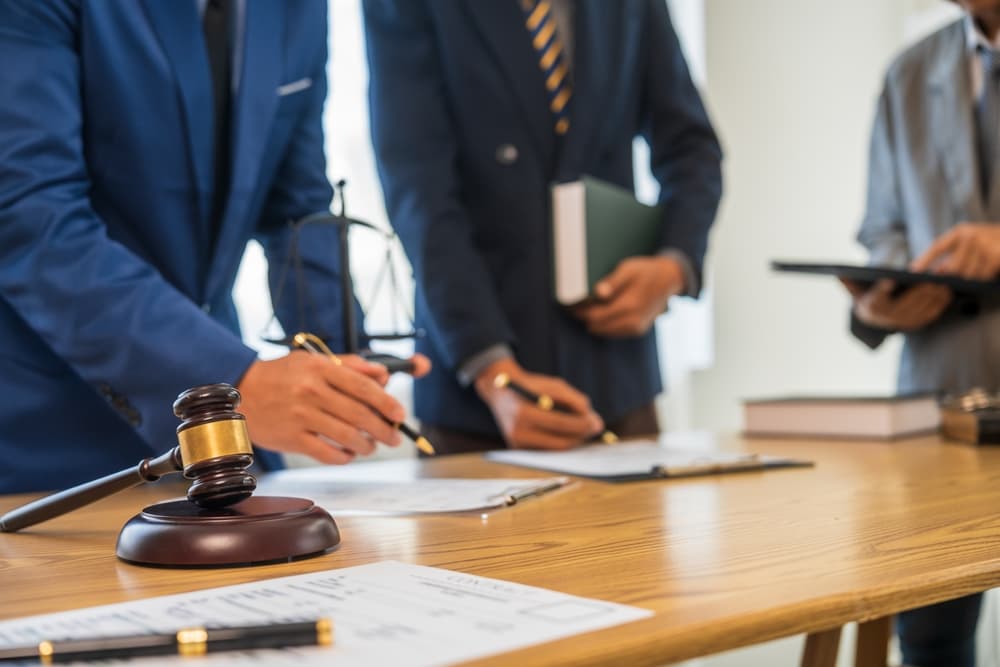 A team of business professionals and a lawyer in formal suits gathers at a desk, discussing a contract and key aspects of law and litigation.