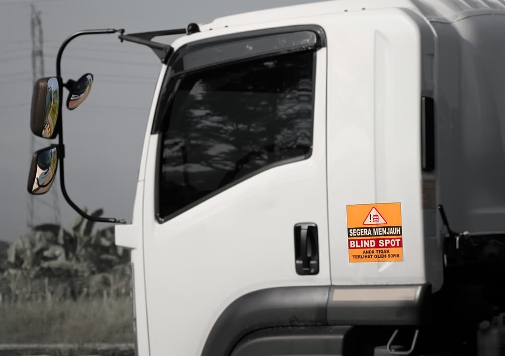 A blind spot sign on a truck, warning drivers to stay clear because they are invisible to the driver. A visible blind spot sticker on the vehicle marks the area of danger.