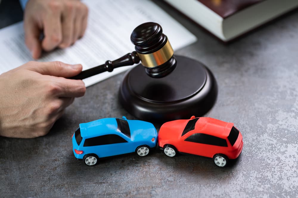 Midsection of a judge striking a gavel near toy cars on a table, symbolizing a car accident legal case.