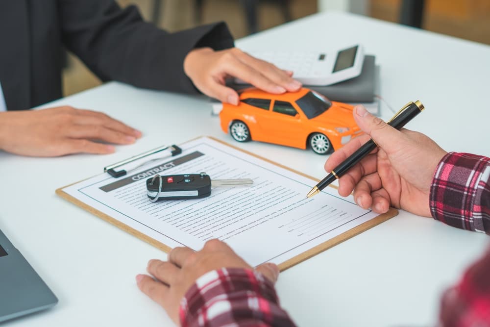 Man signing a car insurance or lease agreement. Writing a signature on a contract with car keys on the table. Concept of vehicle purchase, sale, or warranty.