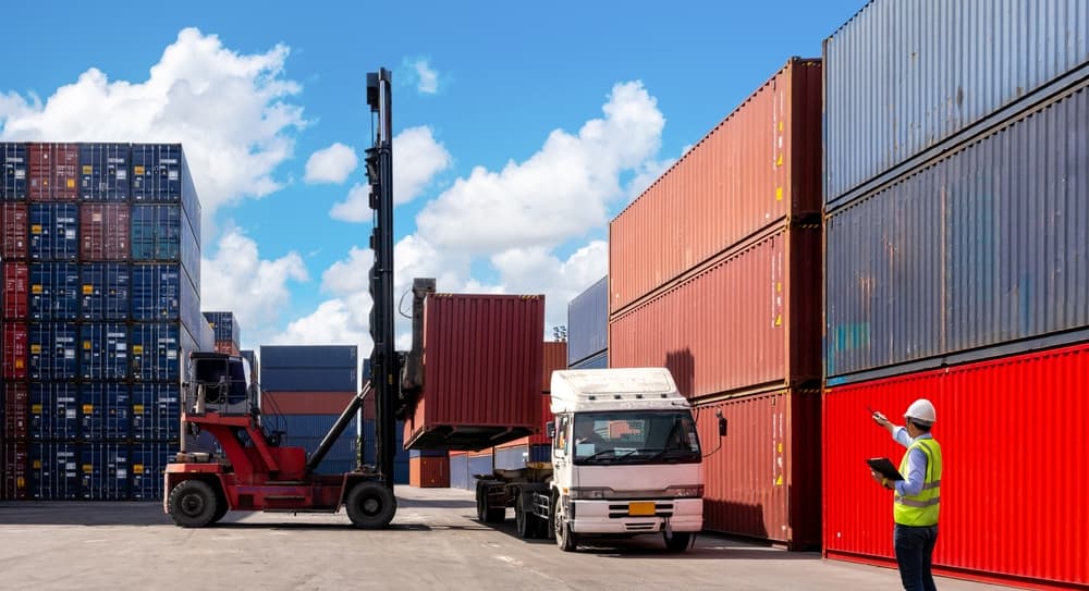 A foreman oversees the loading of container boxes from a cargo freight ship for import and export operations.