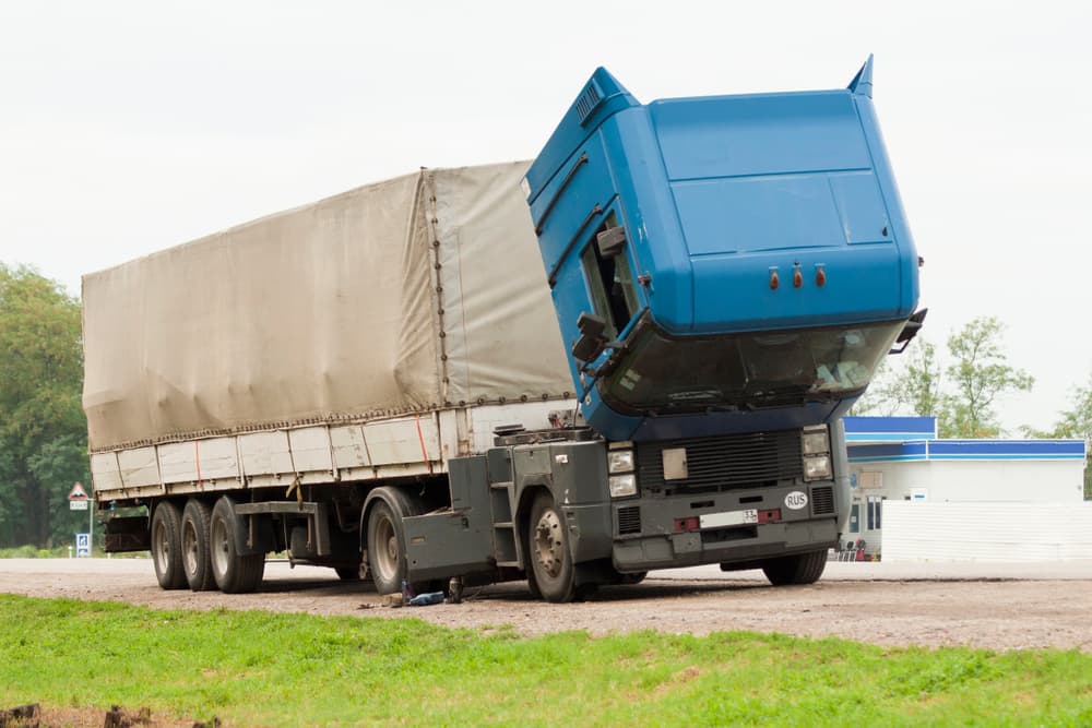 A broken-down cargo truck with its cab raised is parked on the roadside as a mechanical issue is being inspected.