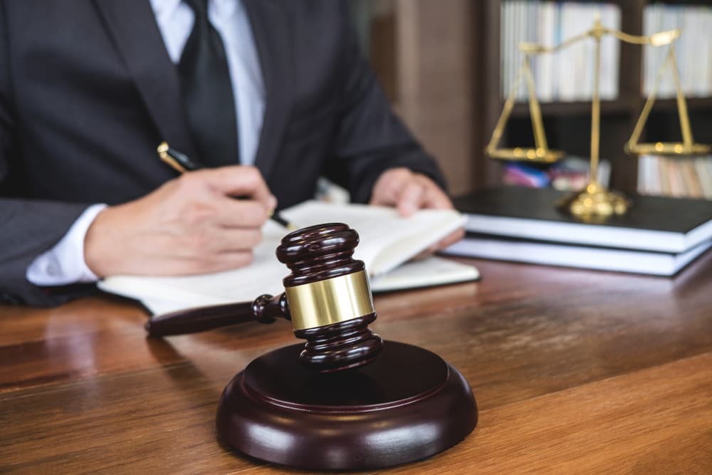 Legal advice and justice concept: A judge's gavel with a lawyer or counselor in a suit, working on documents in a courtroom setting.