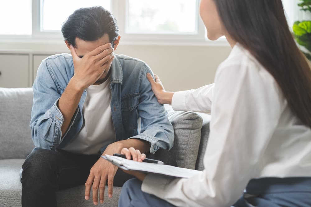 Psychology and depression concept: An Asian young man receives counseling from a psychologist. The doctor takes notes during a mental health therapy session at a clinic.