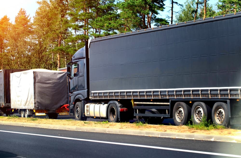 A black semi-trailer truck collided with the trailer of another vehicle on the road. The incident involved emergency braking, failure to maintain proper distance, and took place near a forest.