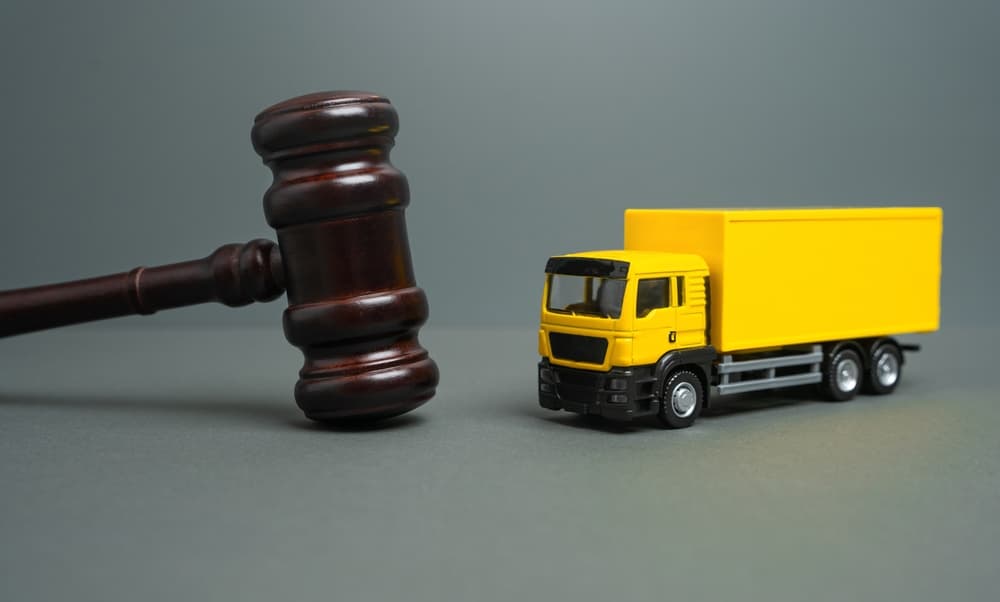 A yellow truck beside a judge’s gavel symbolizes a legal case involving new laws, regulations, and restrictions—possibly tied to the bankruptcy and auction-based sale of a transportation company’s assets.
