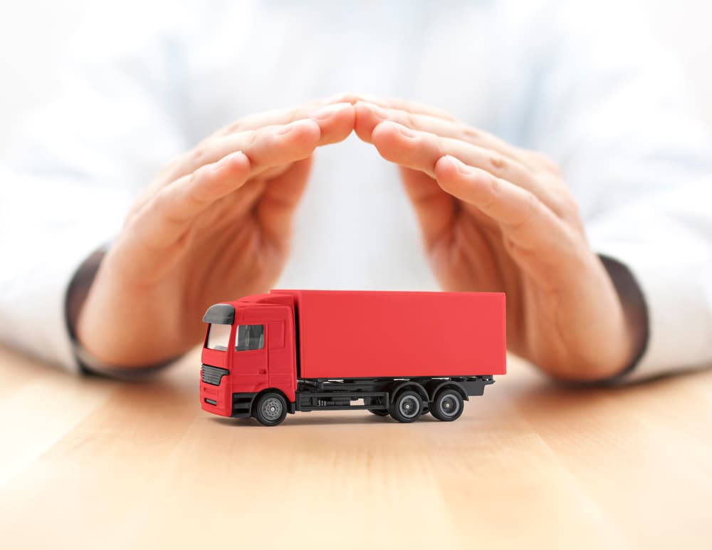 A red semi-truck being shielded by hands, symbolizing protection and security.