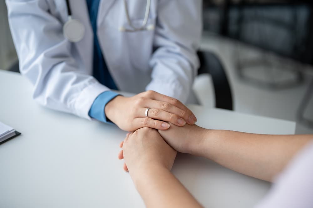 Close-up of a compassionate doctor gently holding a patient’s hands to offer comfort and reassurance during a hospital checkup.