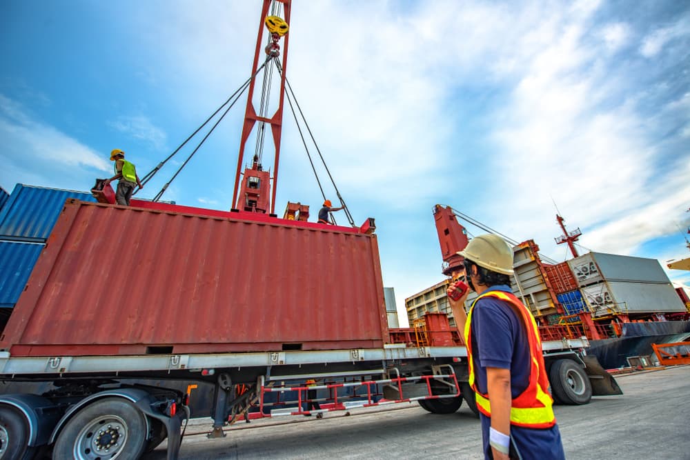A container unit is being lifted and loaded by the ship's crane for bay storage on the cargo carrier, overseen by the loading master, as part of logistics and transport services for worldwide shipment.
