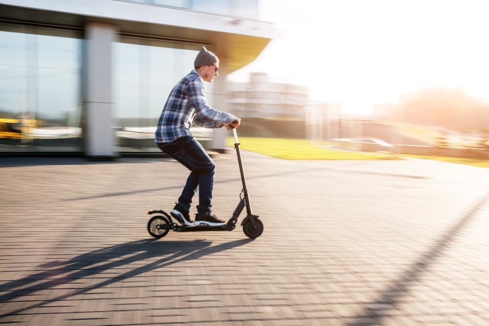 A young man rides an electric scooter at speed on a city street, captured with motion blur to emphasize movement.