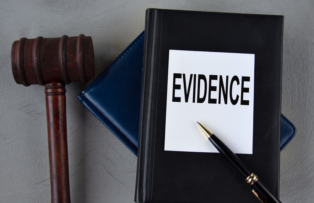The word "EVIDENCE" printed on a white sheet, placed alongside leather notebooks, a judge's gavel, and a pen.