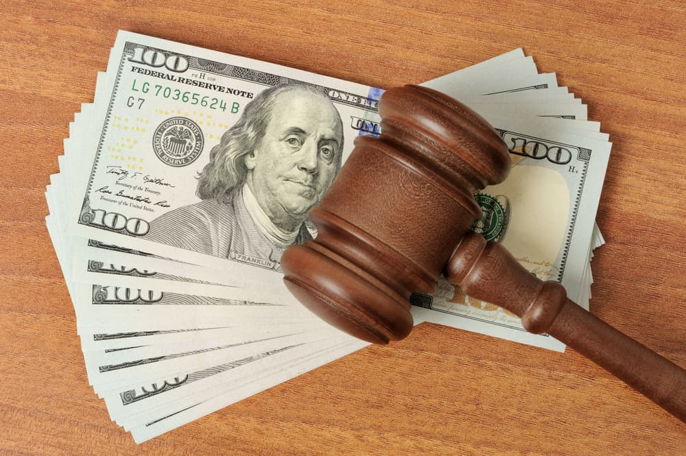 A judge's gavel rests beside a stack of dollar bills, symbolizing financial judgments or legal settlements.
