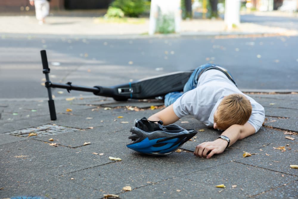 Unconscious man lying on a concrete street following an electric scooter accident.